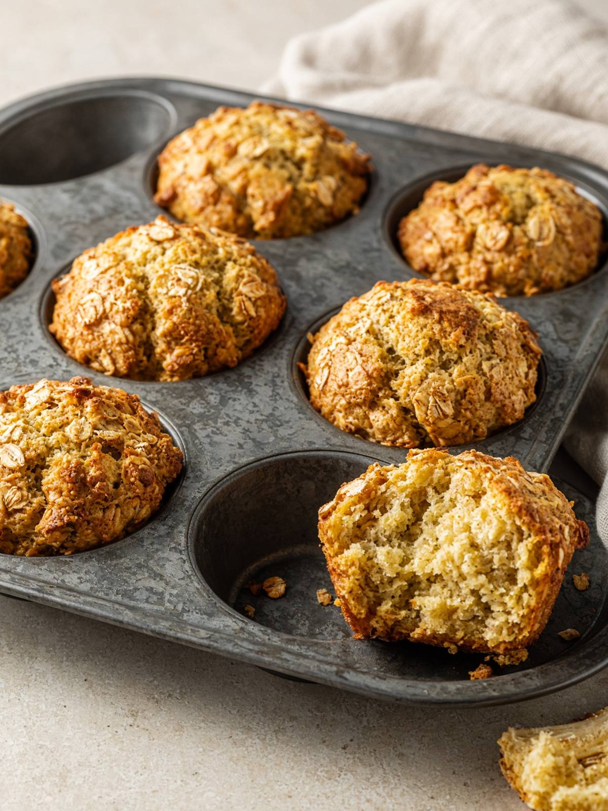 A dozen golden muffins with a cracked top and visible oat flakes.