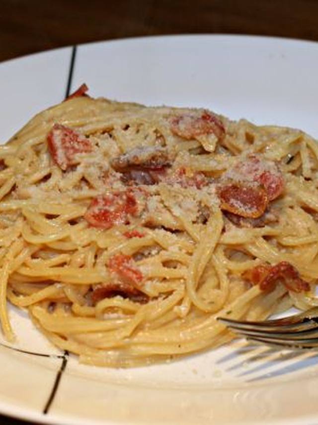 Spaghetti carbonara with bacon bits and green peas on a plate
