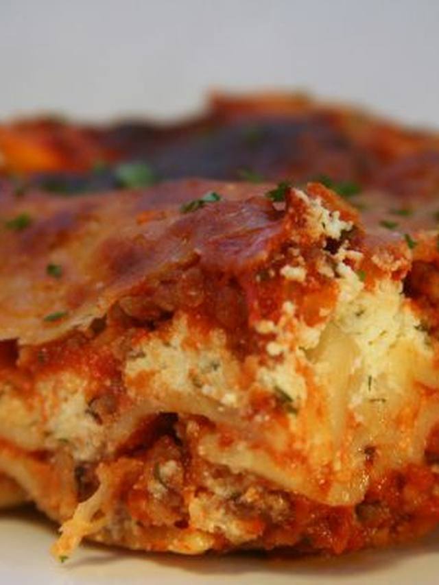 A square of lasagna with melted cheese and a basil leaf