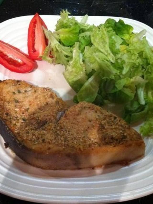 Grilled swordfish steaks with char marks and fresh herbs on a platter