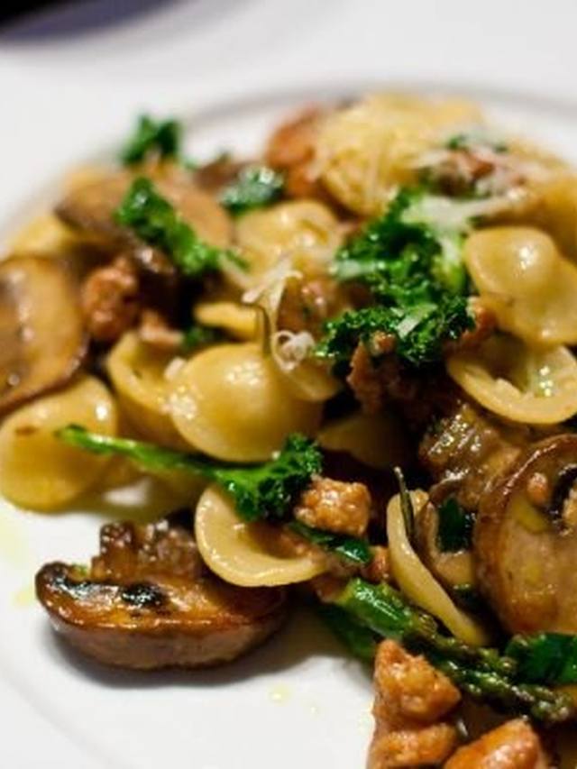 Orecchiette pasta with crumbled sausage and wilted kale in a shallow bowl