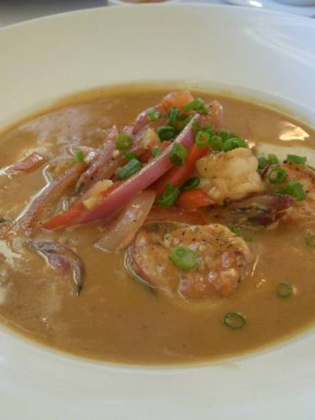 A bowl of creamy grits topped with pink shrimp and sliced sausage