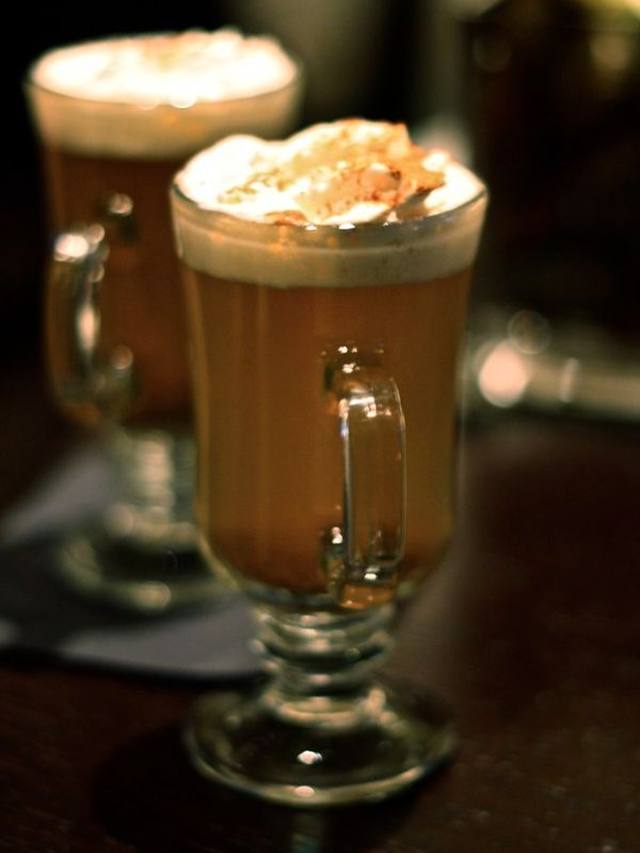 Mugs of spiced apple cider with cinnamon sticks beside a slow cooker