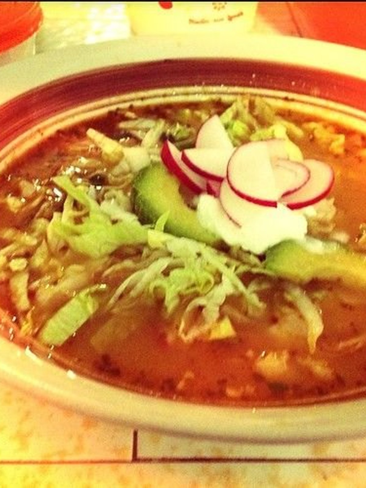 A bowl of red chicken pozole with radish, cabbage, and lime