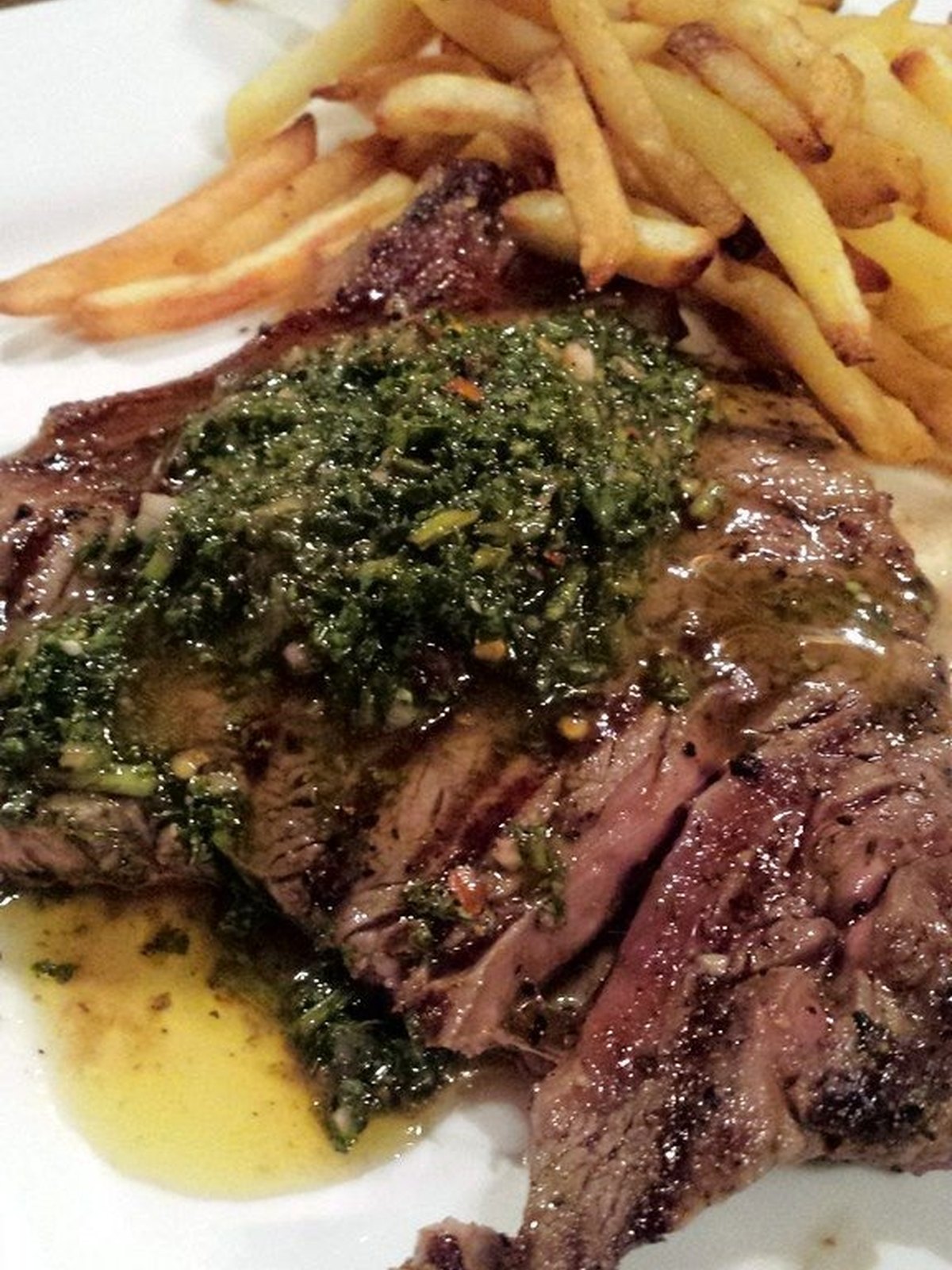 Sliced grilled flank steak topped with green chimichurri