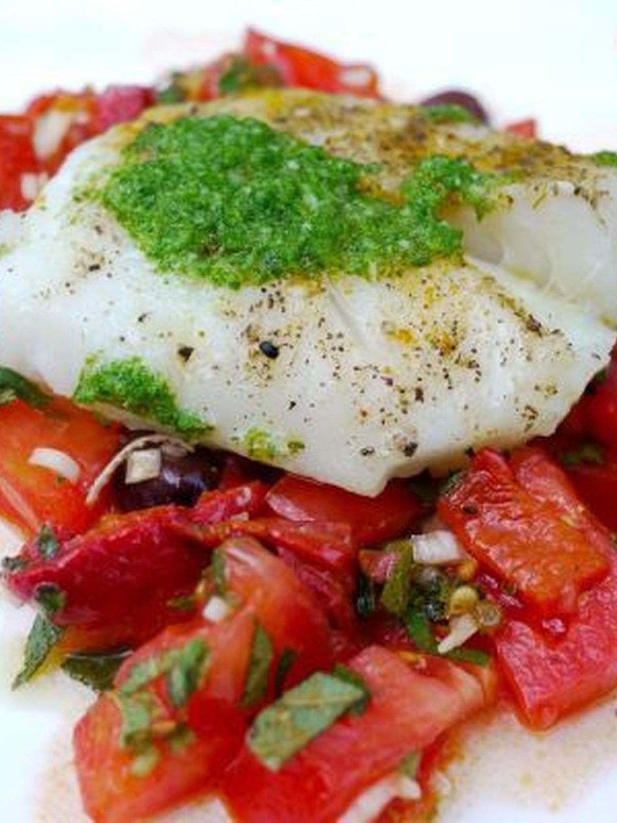 Flaky baked cod with blistered cherry tomatoes and olives on a metal sheet pan
